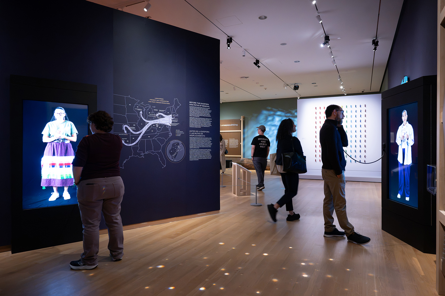 A crowd of visitors interacts with large screens in a gallery with purple walls