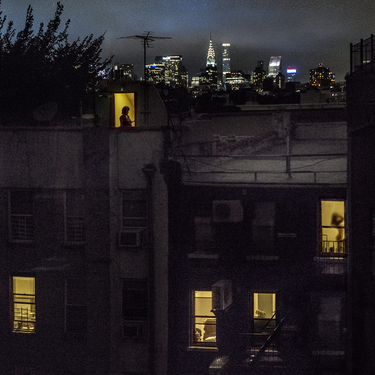 Vista trasera del apartamento de Sally Davies en East 5th Street por la noche con ventanas iluminadas.
