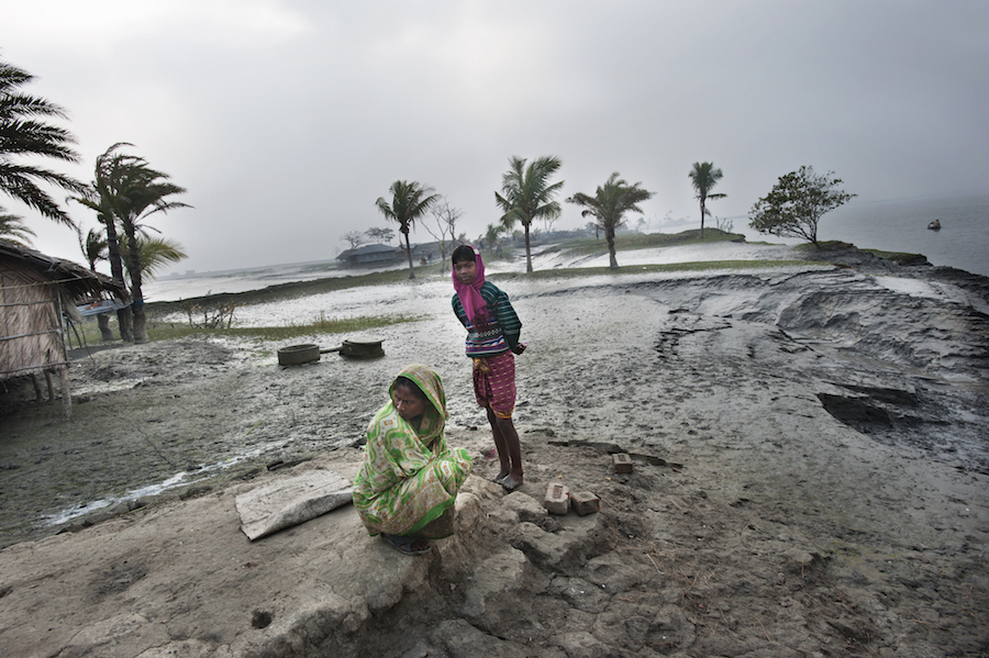 A mother (sitting) and her daughter (standing) in their former village of Bainpara among ruined homes and destroyed landscape.