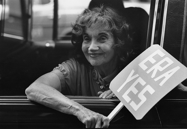 Alice Paul looks out of the window of a vehicle holding a sign that reads "ERA YES"