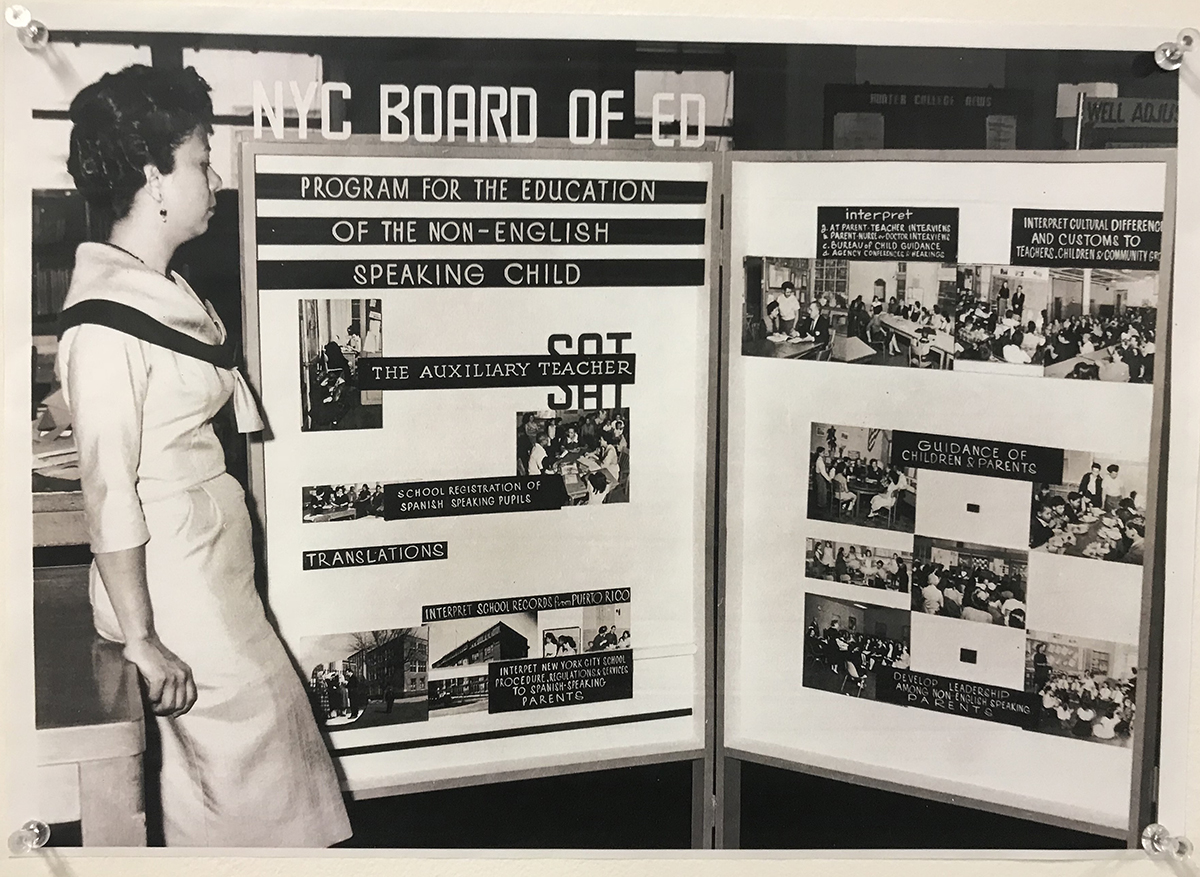 A woman stands in front of a Recruitment Board for Spanish-speaking Substitute Auxiliary Teachers in New York City public schools.  