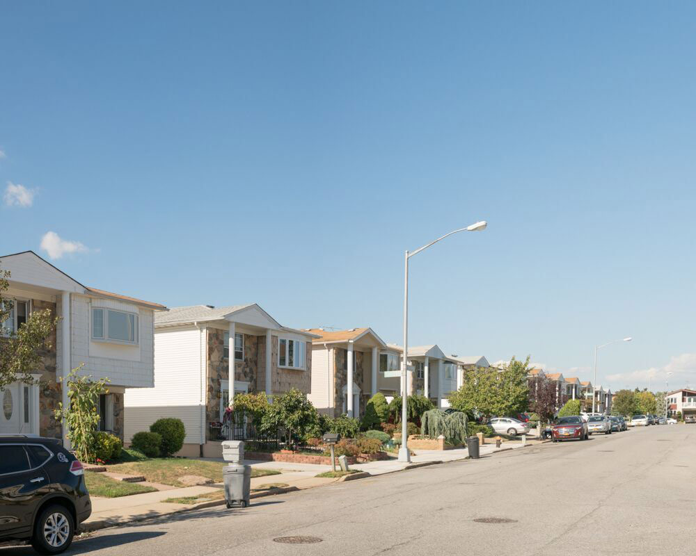 Uma série de casas idênticas de dois andares se alinha em uma rua