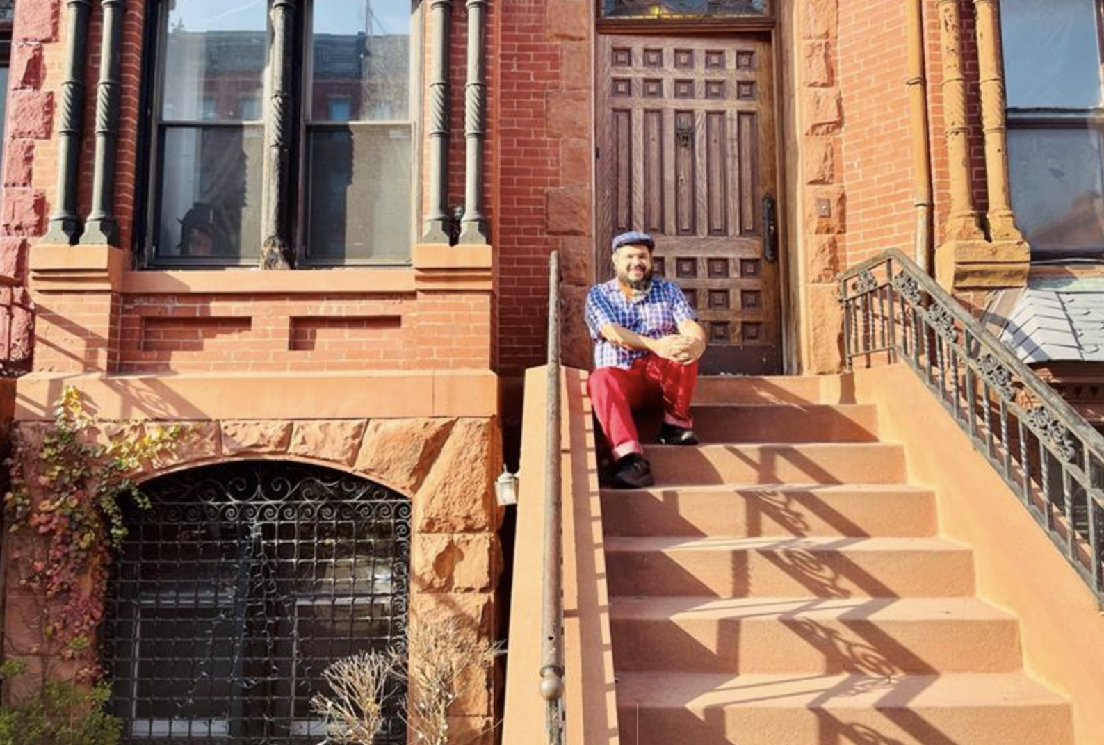 Monxo López sentado na escada em frente a uma casa de arenito