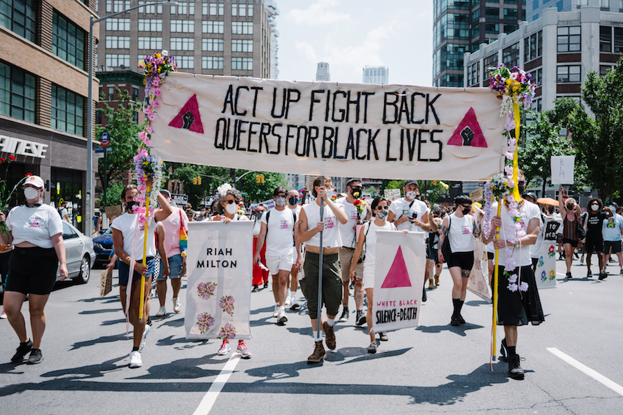 Um grupo de participantes da Marcha de Libertação Queer para Vidas Negras e Contra a Brutalidade Policial carregam uma placa que diz "Act Up Fight Back Queers for Black Lives"
