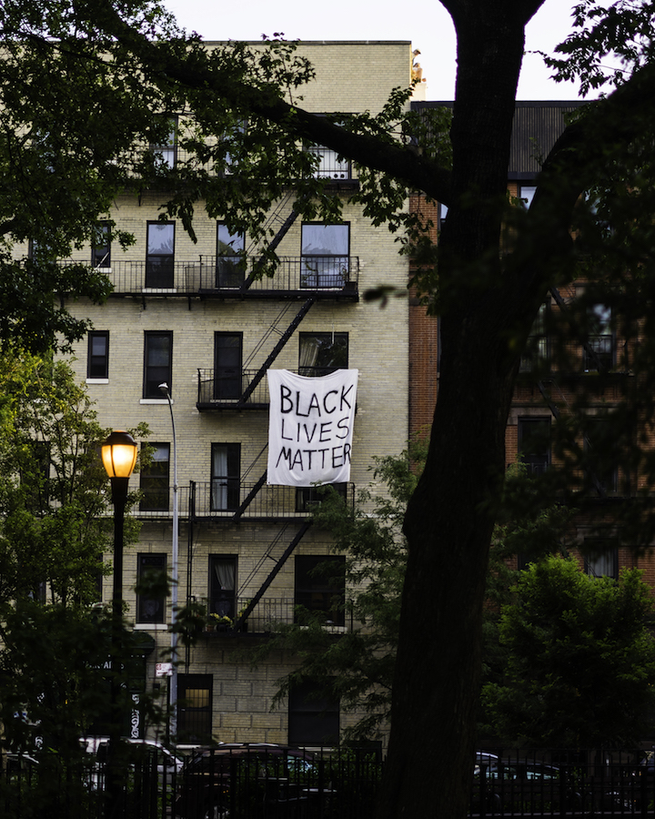 An apartment building with a banner hanging off a fire escape on one of the upper floors reads "Black Lives Matter."