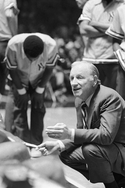 Imagen del entrenador de los Knicks, Red Holzman, arrodillado y hablando con los jugadores en la cancha.