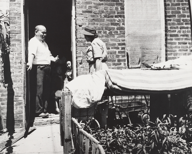 一个男人带着一个小孩站在门口。 一位女士正在砖房外与他们交谈。