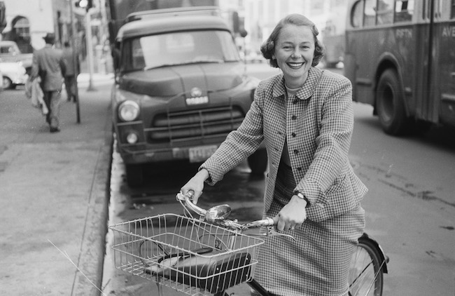 Fotografia de uma mulher andando de bicicleta na rua em frente a um caminhão.