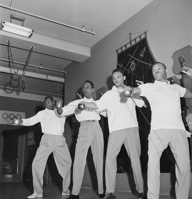 Photo en noir et blanc de quatre hommes tenant des sabres alignés.