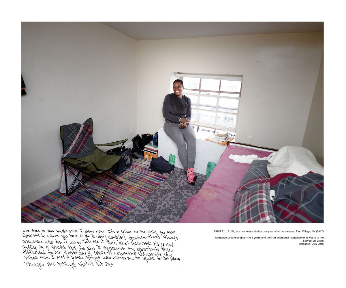 A woman sits a window in a bedroom.