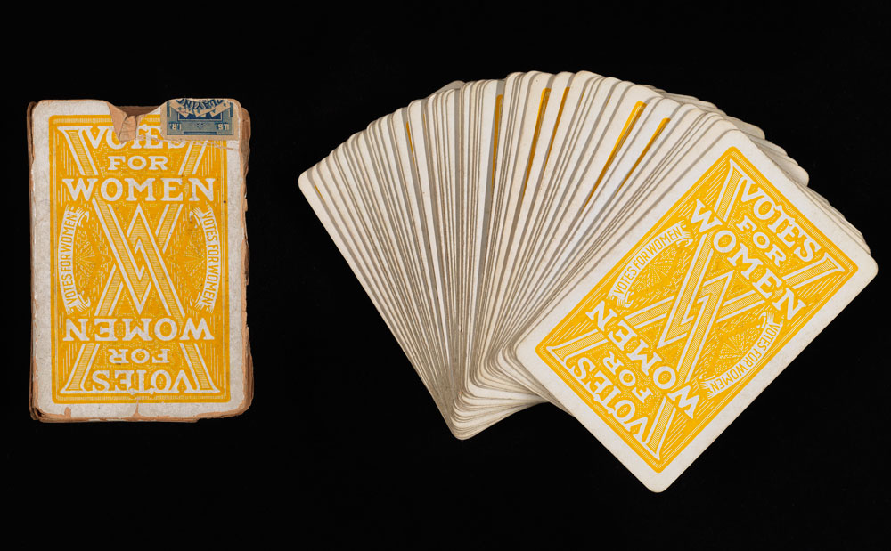 Deck of playing cards. The backs are yellow and say “VOTES FOR WOMEN” with two interlocking “V”s 