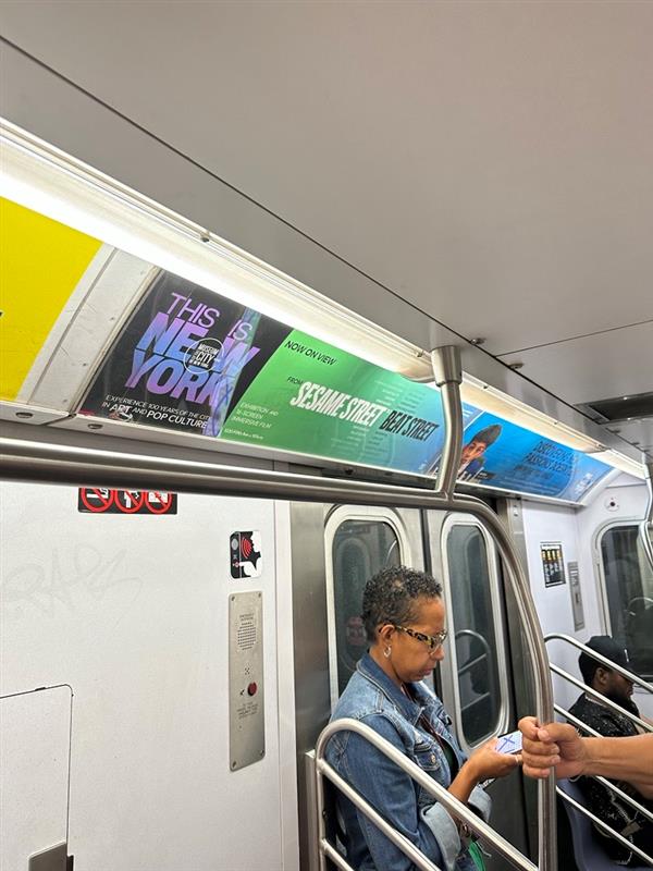 Subway ad for the exhibition "This Is New York" above the door in a subway car.