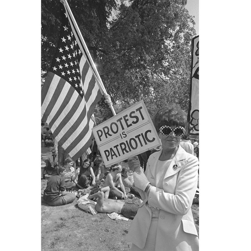 Una fotografía del libro The Activist's Media Handbook, David Fenton. Una mujer sostiene un cartel que dice "La protesta es patriótica" y la bandera de EE. UU.