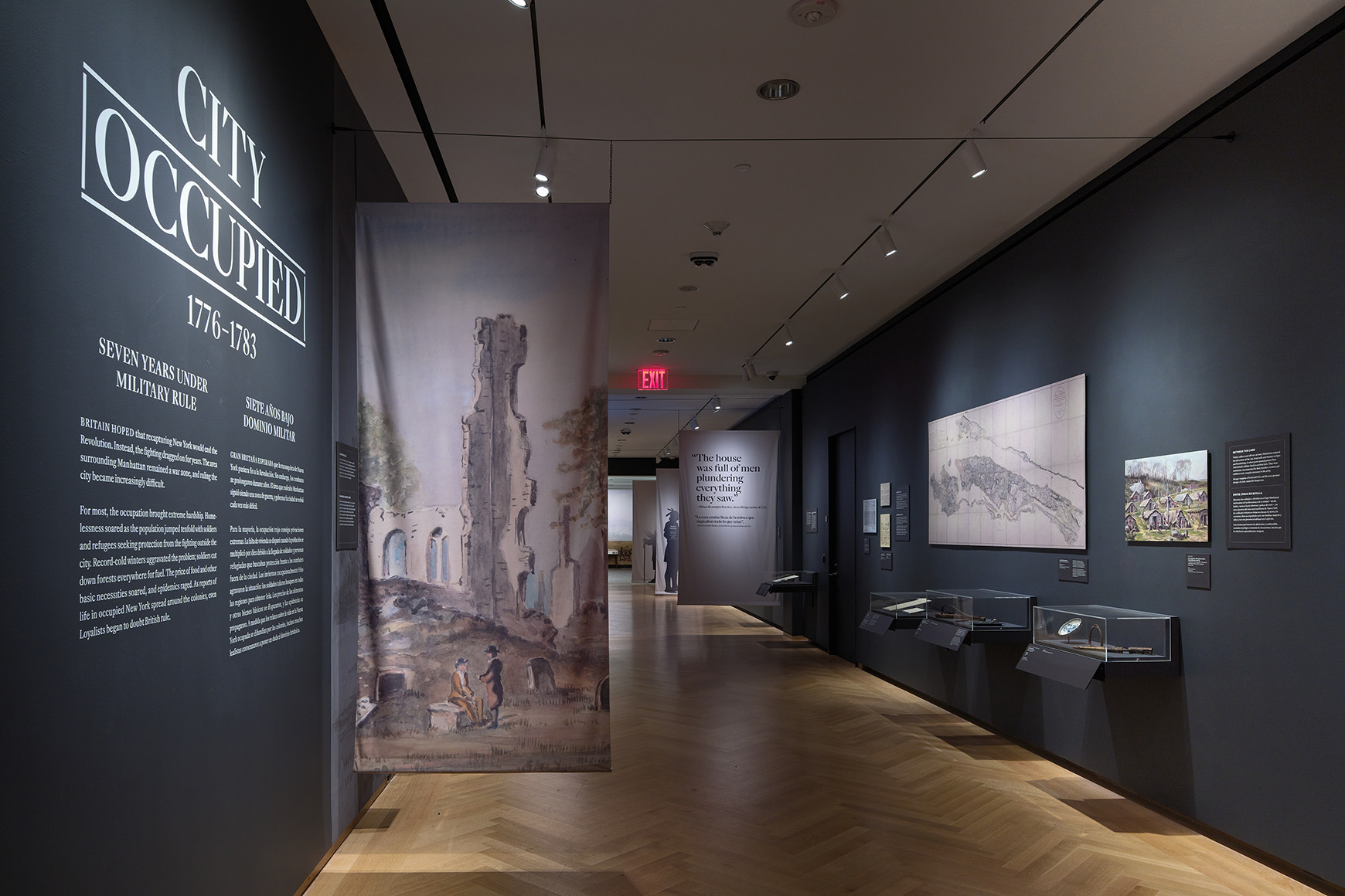 Installation view of the galleries, showing hanging banners, artwork on the walls, and wall text saying, “City Occupied.”