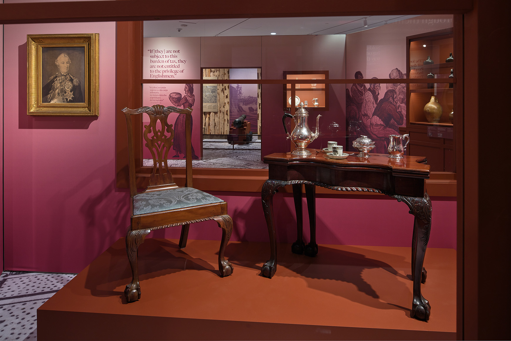 Installation view of the galleries, showing a chair and table set with historic objects, next to artwork on the walls.