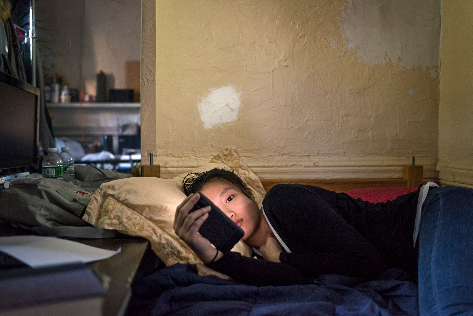 젊은 중국 여자는 그녀의 전화를 쳐다보고 침대 또는 소파에 놓여 있습니다.