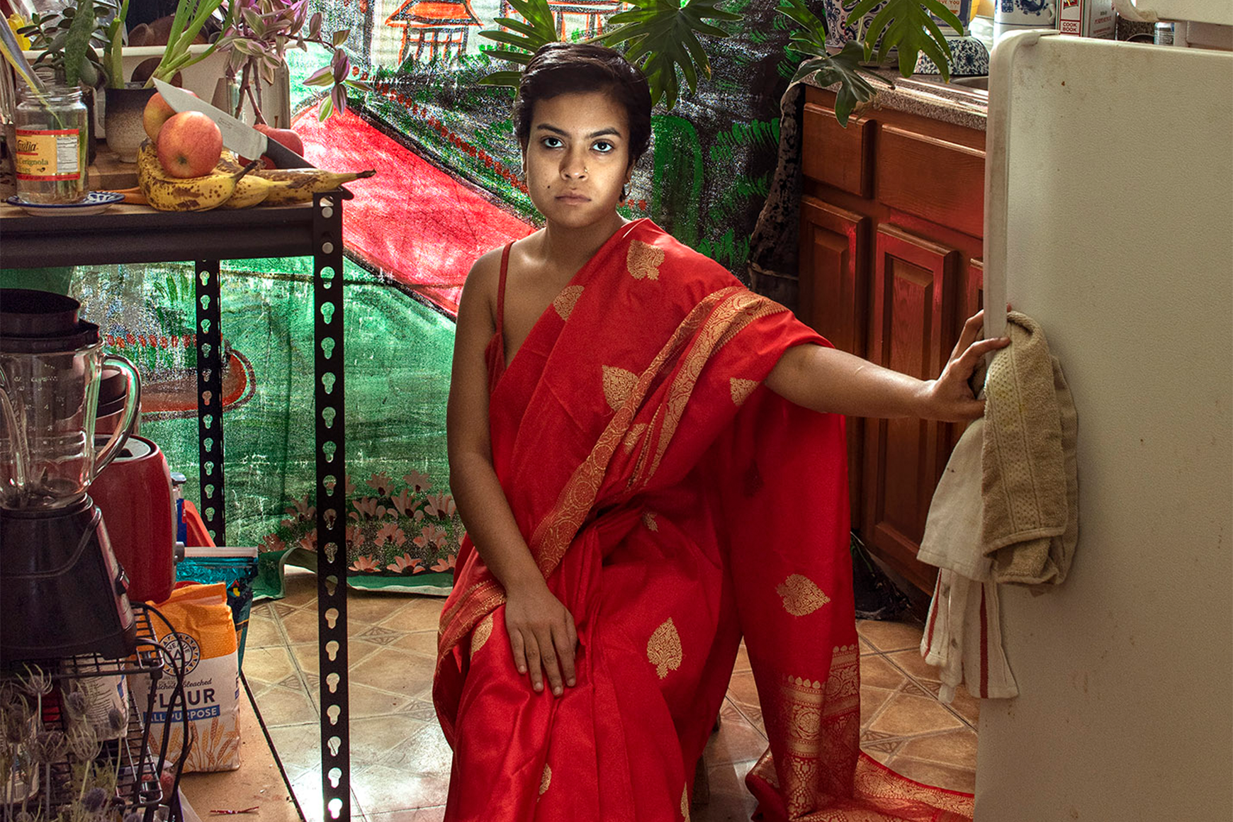 Image of Women sitting on a chair in a kitchen wearing a red dress with their hand on an open refrigerator door.