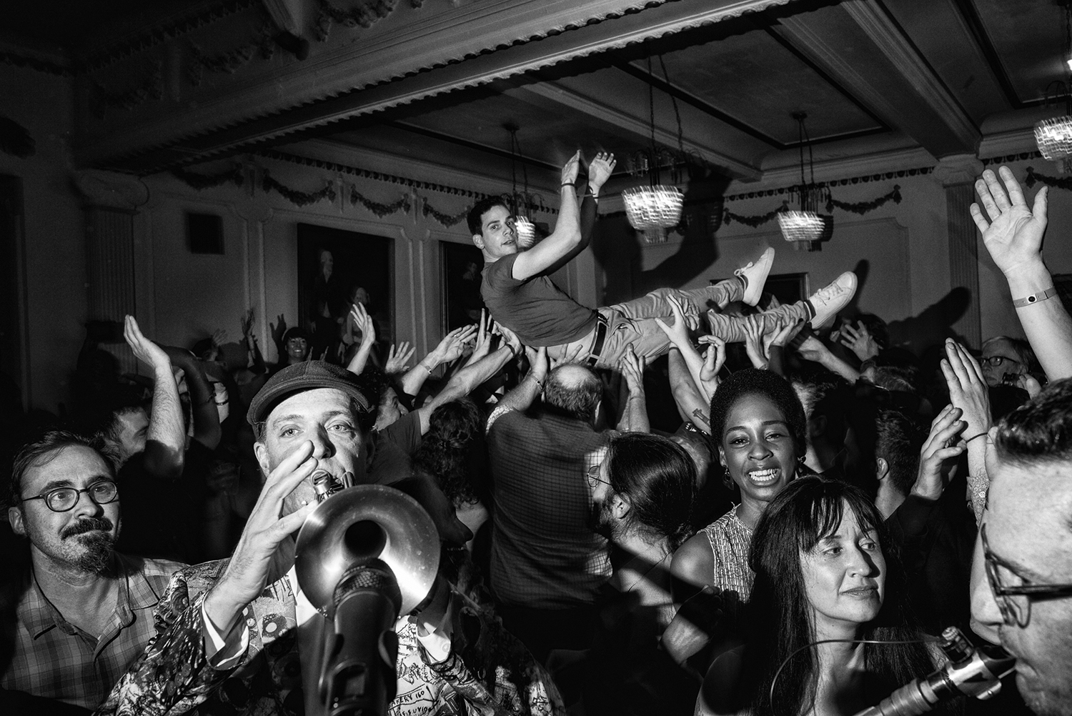 A crowd of people, including two people playing instruments in the foreground and a man crowdsurfing in the background