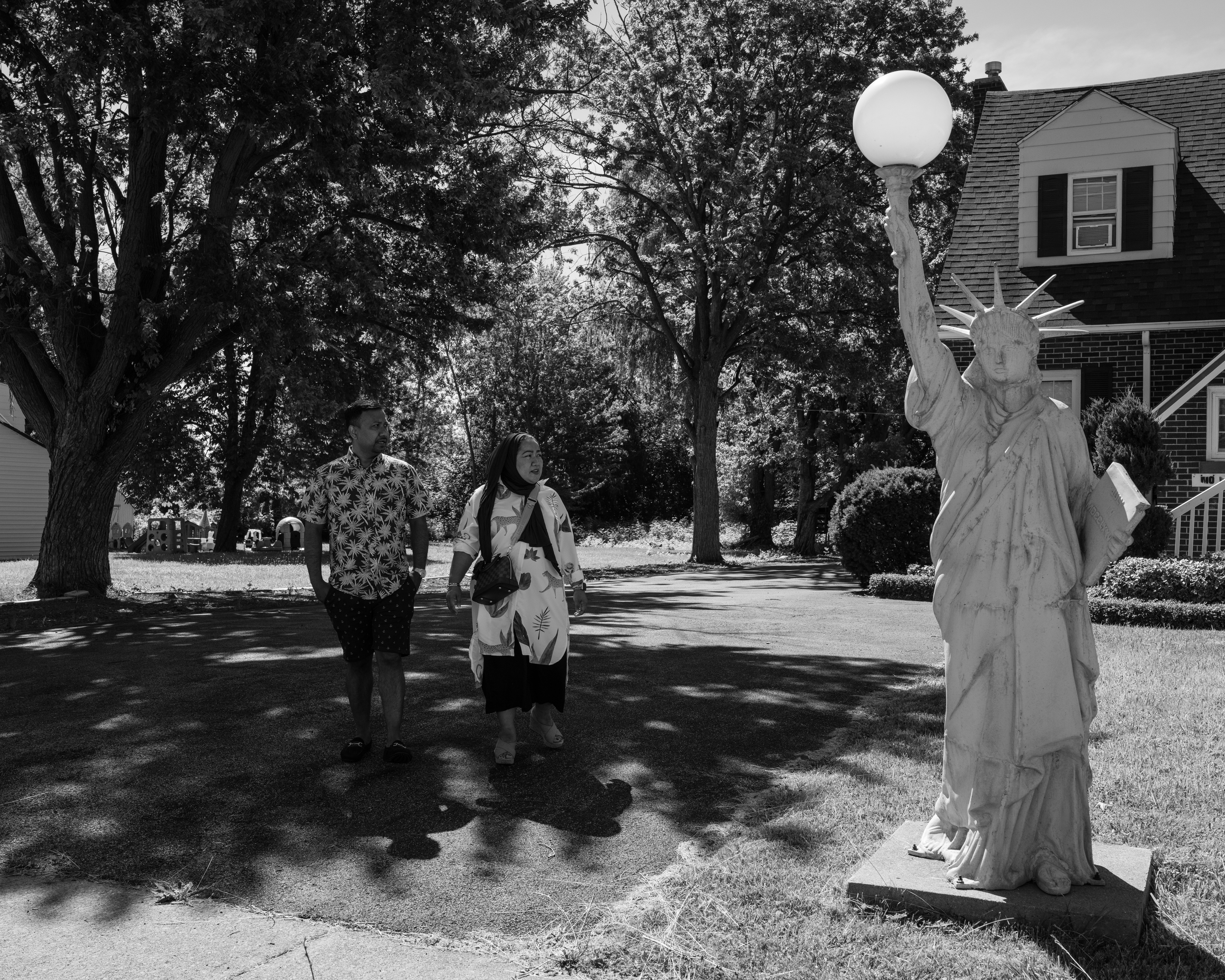 Um homem e uma mulher estão em um gramado ao lado de uma pequena réplica da Estátua da Liberdade.