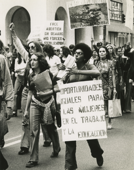 Women march in the streets, some with signs, as part of the Women’s Strike for Equality March