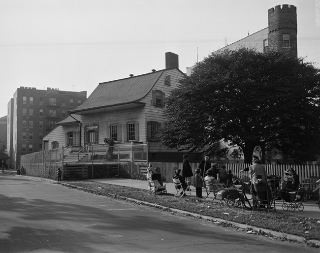 Pessoas sentadas em cadeiras na calçada ao lado da casa de Johannes Van Nuyse, no número 150 da Amersfort Place.