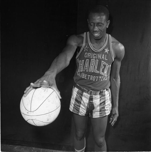 A man wearing a Harlem Globetrotters uniform stands and holds a basketball in one hand. 
