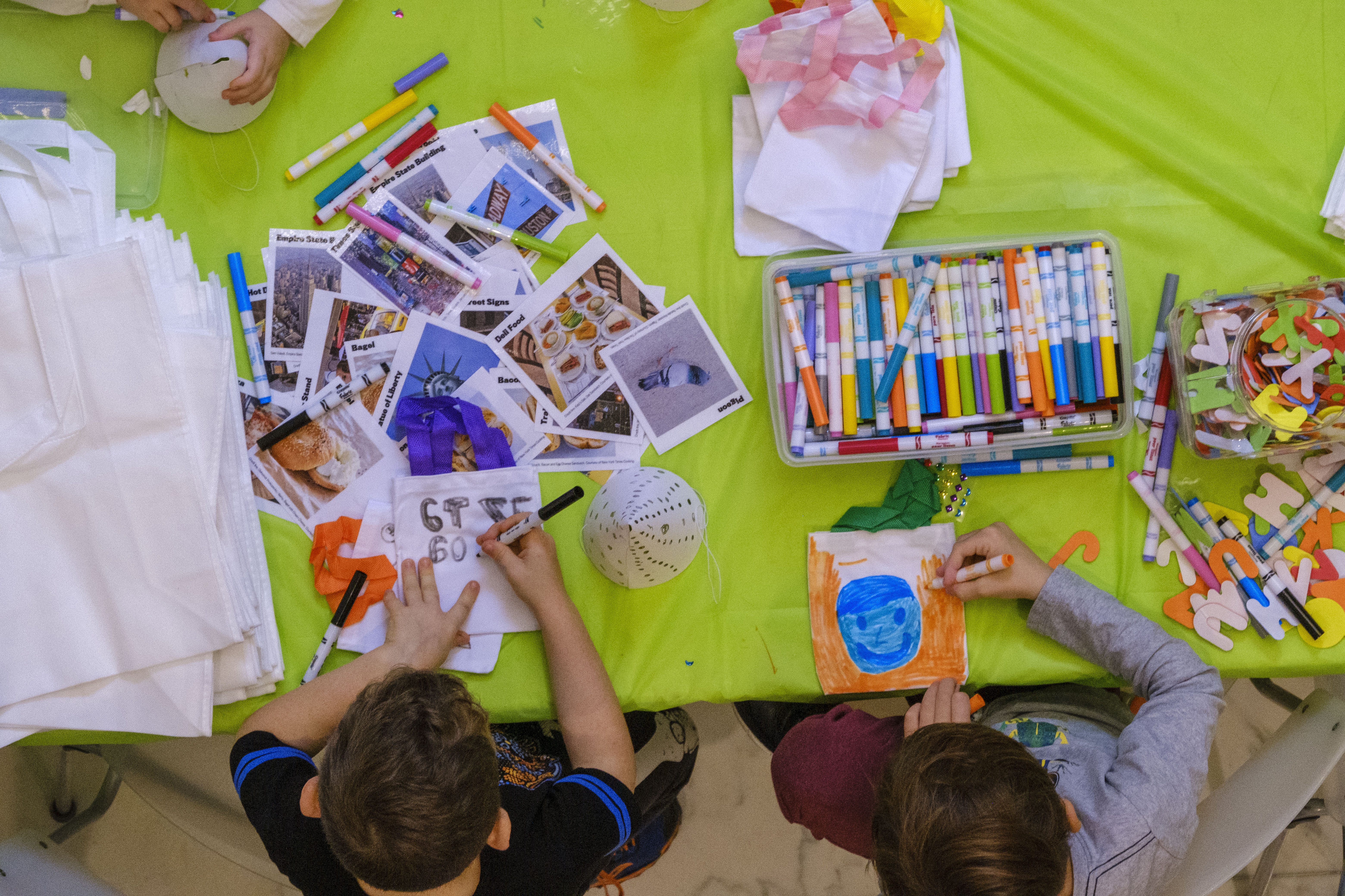 Toma aérea cenital de dos niños coloreando con marcadores y otros materiales de arte coloridos en una mesa a su alrededor.