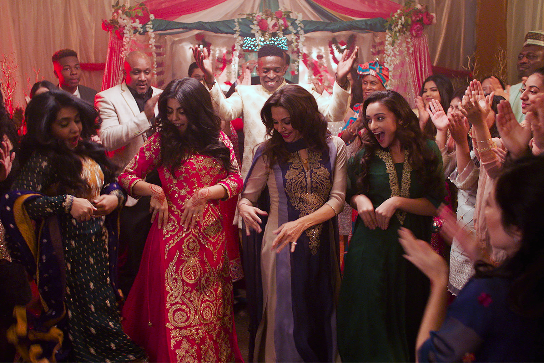 Imagen de un grupo de personas bailando en una sala de fondo rojo durante una ceremonia de boda