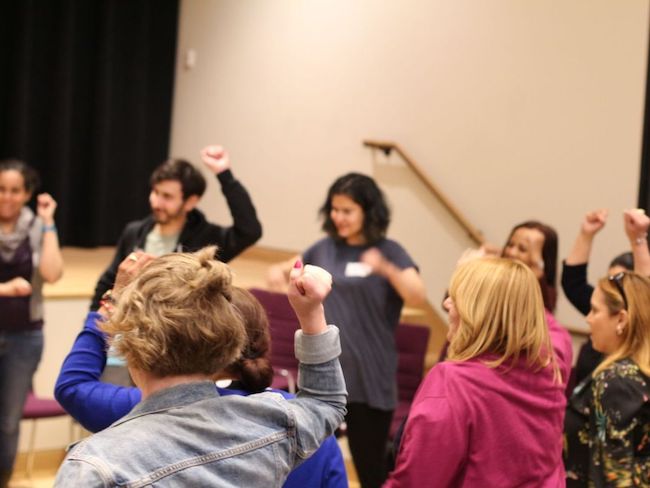 A group of people stand in a circle, some with their arms raised.