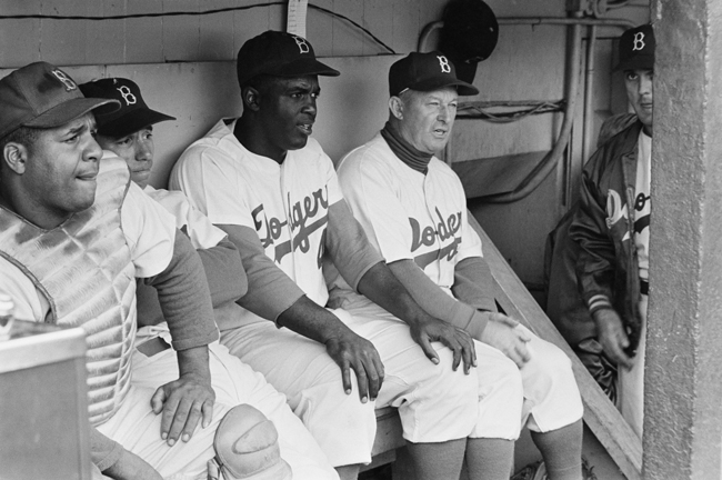 Jackie Robinson se sienta en el refugio de los Dodgers con otros jugadores y el manager Charlie Dressen durante un juego.