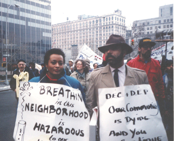 A man and a woman holding posters for an environmental protest stand in a crowd on a NYC street