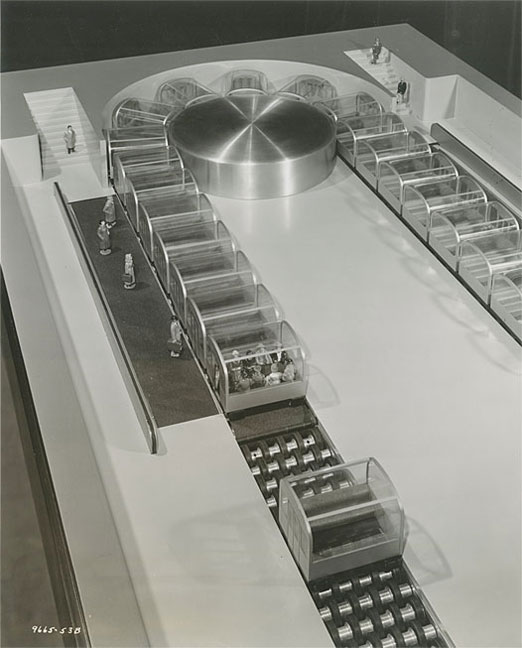 Close-up of working model of conveyor subway system, shows passengers entering and riding in passenger cars.