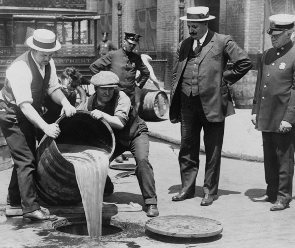 Le commissaire de police adjoint de la ville de New York, John A. Leach (à droite), regarde des agents verser de l'alcool dans les égouts