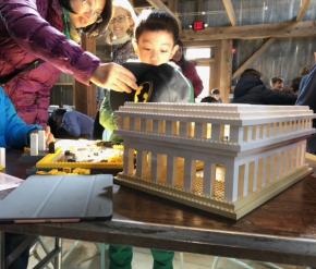Picture of family of mother, boy, and child with an onlooker behind looking in awe at a LEGO construction