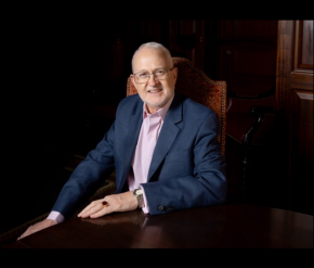 A man in a blue suit sitting in a formal board room
