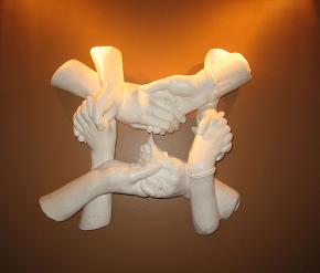 四只白色石膏雕刻的手相互交扣并相互握着，背后闪烁着柔和的黄色光芒。