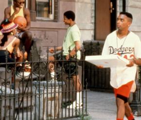 Spike Lee as Mookie walks down a Bedford-Stuyvesant street carrying a pizza