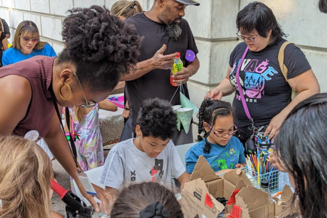 A group of young people stand around a table making crafts with instructors.