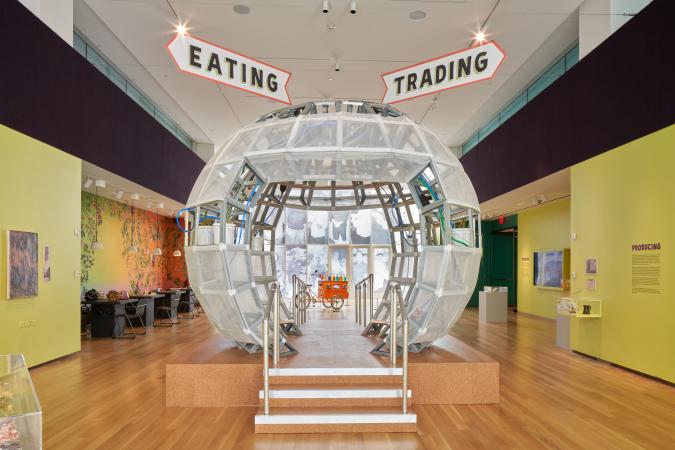 Una gran esfera transparente, similar a un globo de nieve, se encuentra en el centro de la imagen con letreros que dicen "comer" y "comerciar" encima.