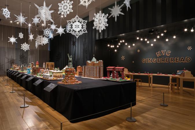 A long table with gingerbread houses inspired by New York, with lights and snowflakes hanging above