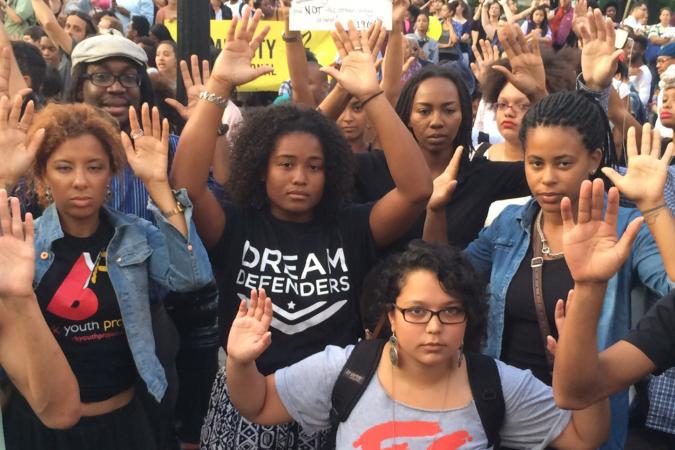 Manifestantes da Black Lives Matter com as mãos no ar em sinal de rendição e o slogan "mãos para cima não atiram"