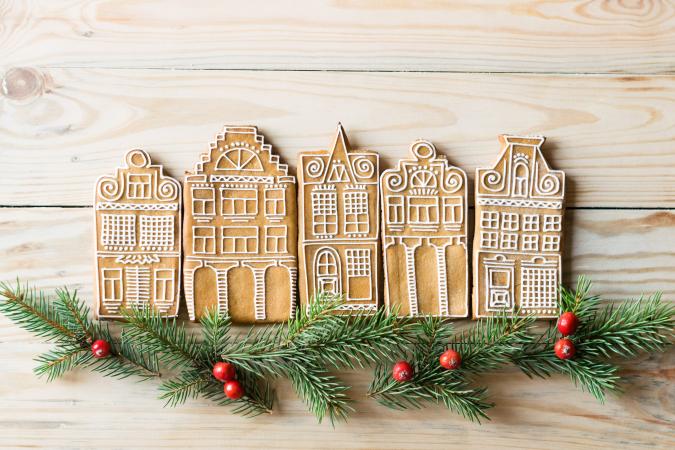 Five homemade gingerbread houses standing in a row with fir-tree branches and berries on wooden 