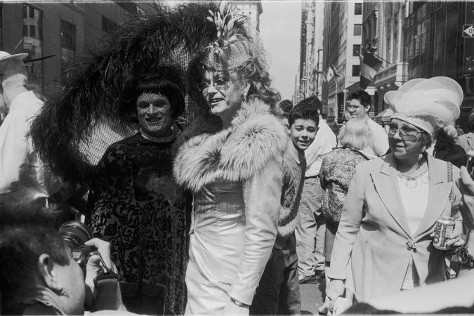 Two drag queens posing for a photo with an older woman watching