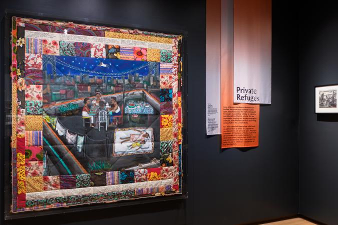 A large colorful quilt hangs on the wall of a gallery.