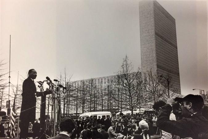 From an elevated platform, Rev. Martin Luther King Jr. addresses a gathered crowd of journalists in New York City