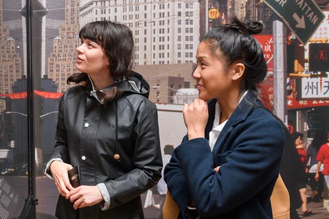 Two people in front of a photograph of New York City, looking at exhibition objects