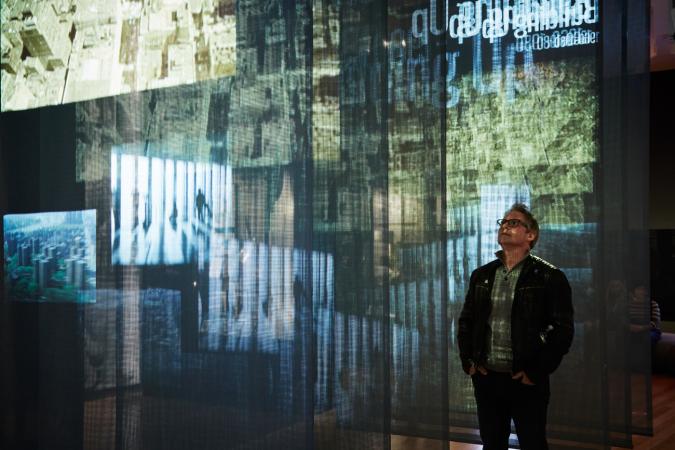 A visitor stands in-between sheer panels as a video projection plays across them