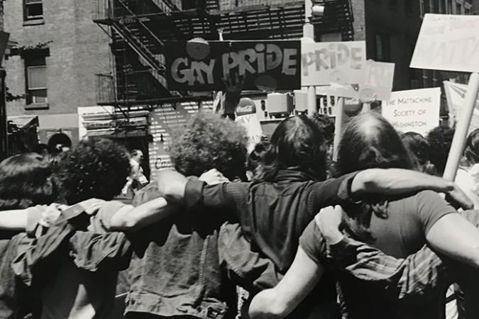 Photograph by Fred W. McDarrah of a group of people with their arms around each other and holding signs related to Pride