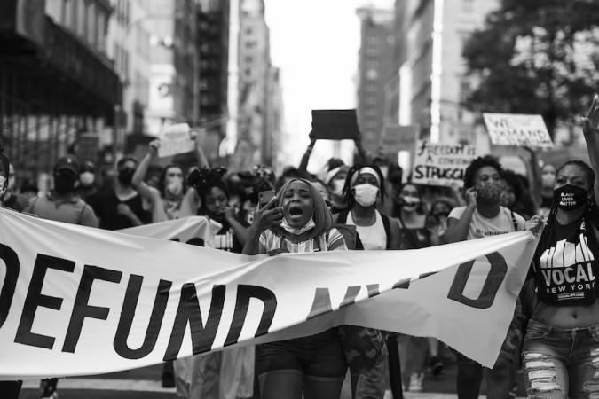 Uma multidão de manifestantes segura uma placa que diz "DEFUND NYPD"