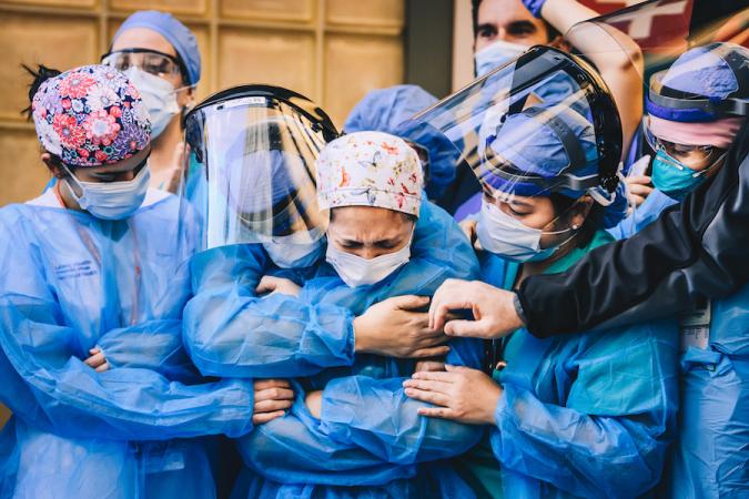 Un grupo de trabajadores médicos se para abrazados usando EPP que incluyen máscaras, protectores faciales y batas.